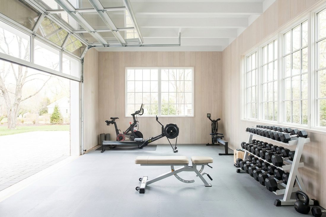 A bright converted garage home gym with a bench and a rack of dumbbells